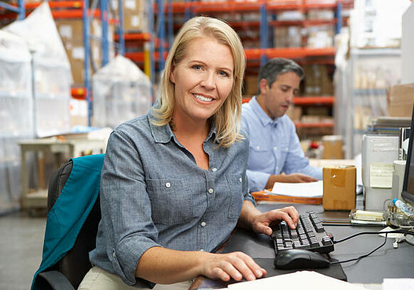 Businesswoman Working At Desk In Warehouse Smiling To Camera
